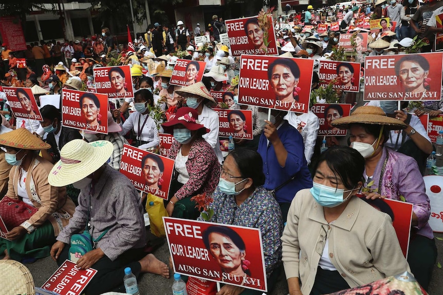 A large crowd of sitting protesters hold images of Aung San Suu Kyi during an anti-coup protest.