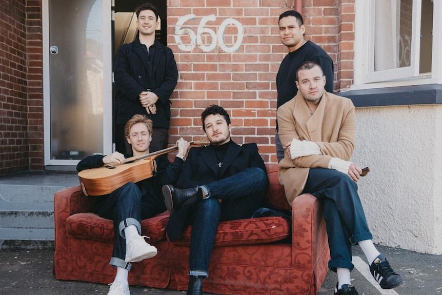 Three men sit on a red couch in front of two other men outside a brick building with 660 painted on the wall 