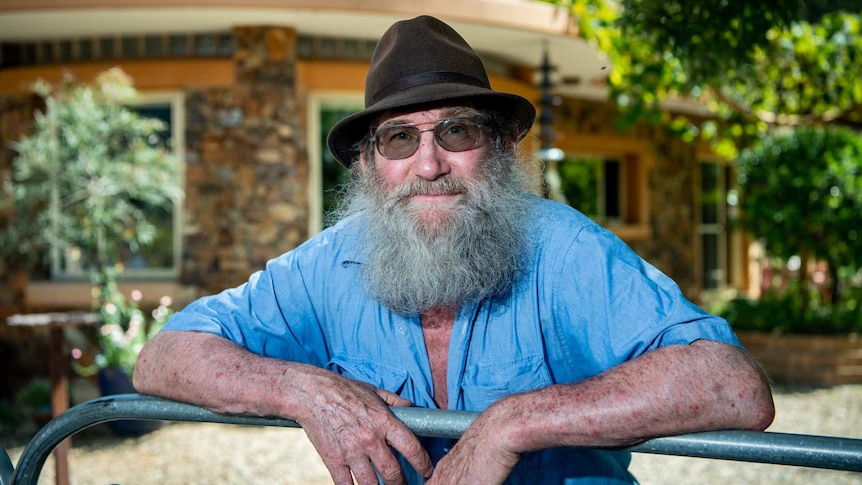 Don Firth leans on his front gate in front of his stone house, which is built into the side of a hill.