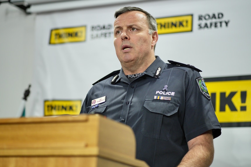 A policeman stands in front of road safety messaging while talking to the media at a podium