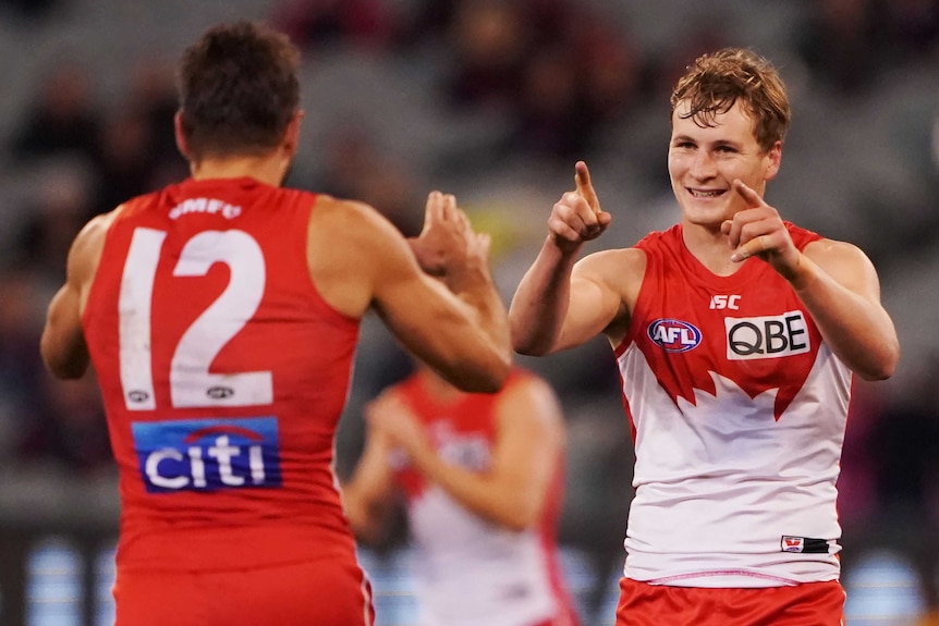 An AFL player points to a teammate in celebration after kicking a goal.