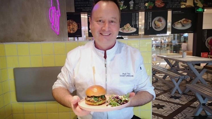 Queensland chef Paul Tait holds a plate filled with a hot pot Aussie burger in a restaurant.