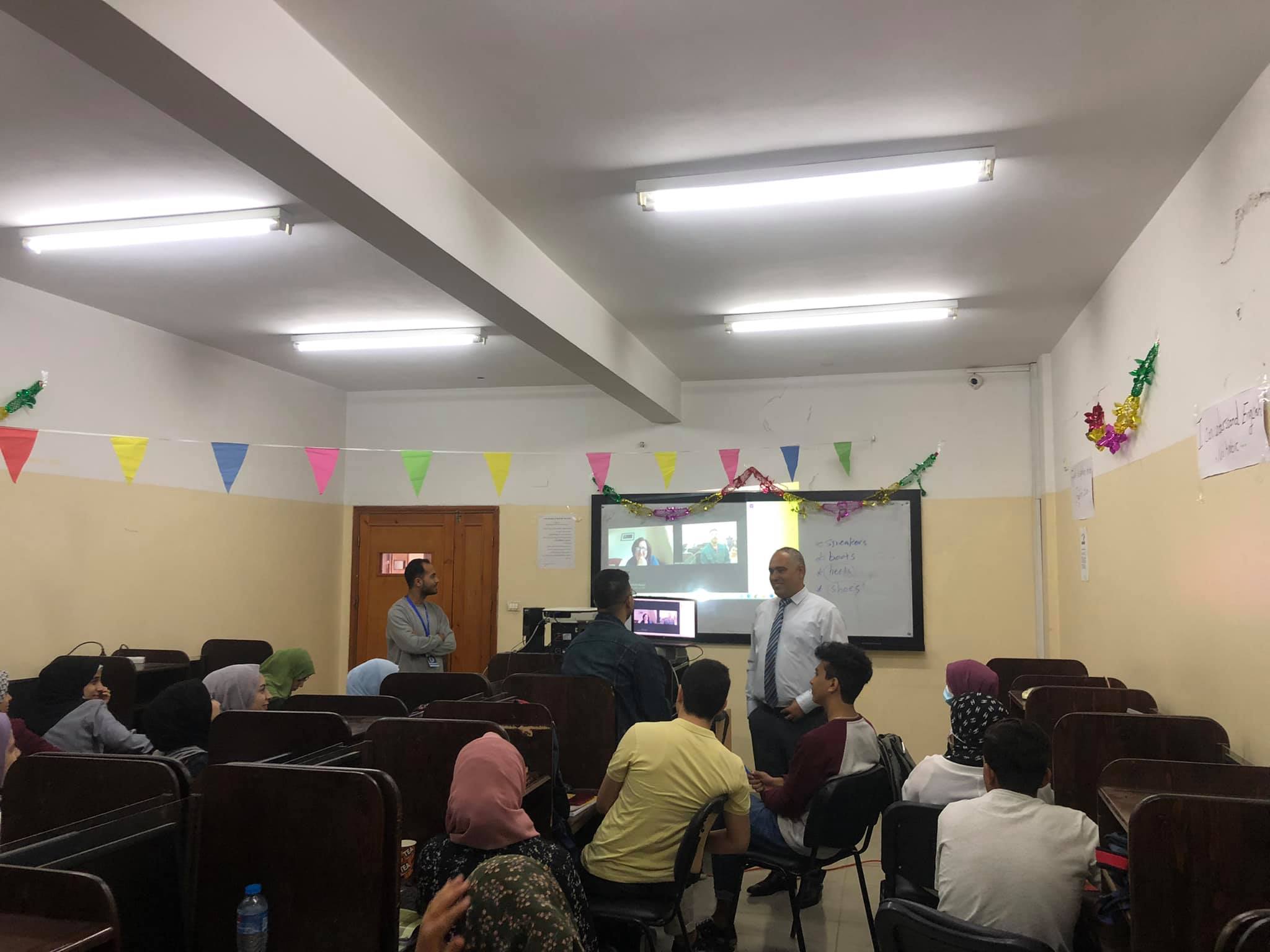 A middle aged man stands in front of a classroom, teaching students.