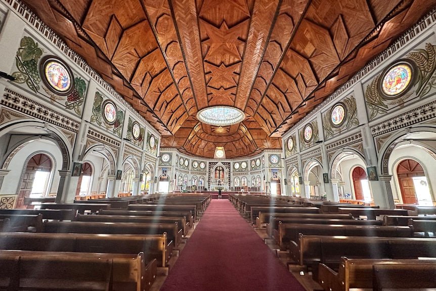 Rows of pews under  wooden ceiling carved in traditional Samoan shapes and patterns, in the Immaculate Conception Cathedral.