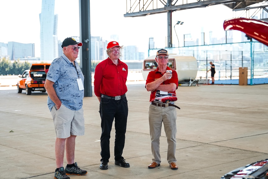 Three men standing in a large hangar.