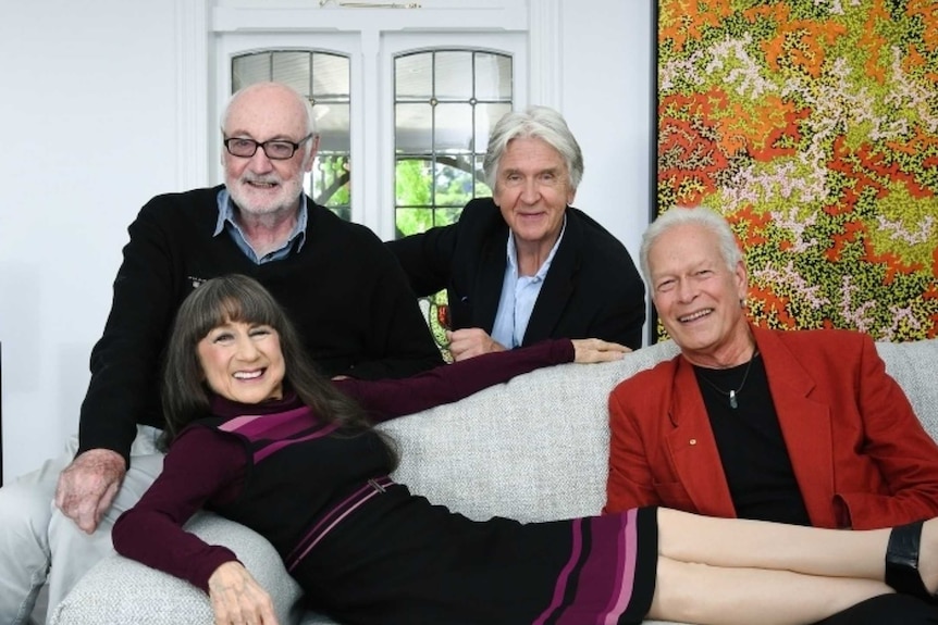 A woman lays on a white couch surrounded by three older men 