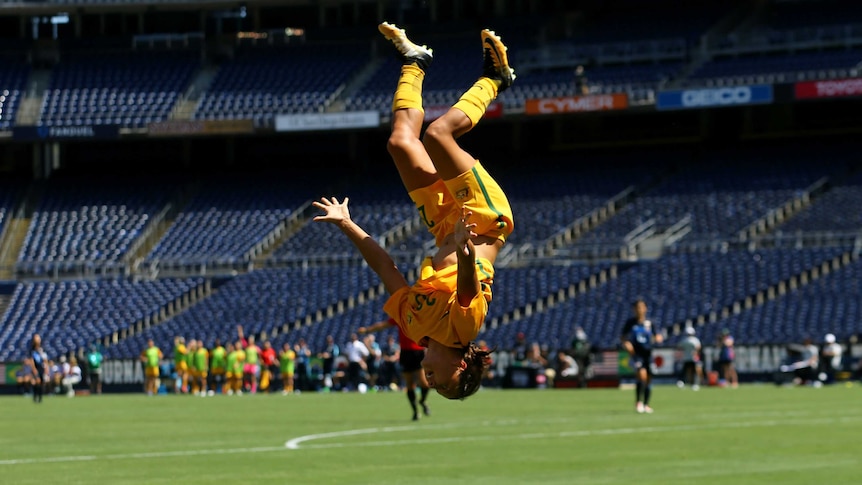 Australian footballer Sam Kerr is upside-down, in mid-back flip.