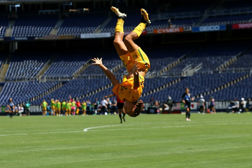 Australian footballer Sam Kerr is upside-down, in mid-back flip.