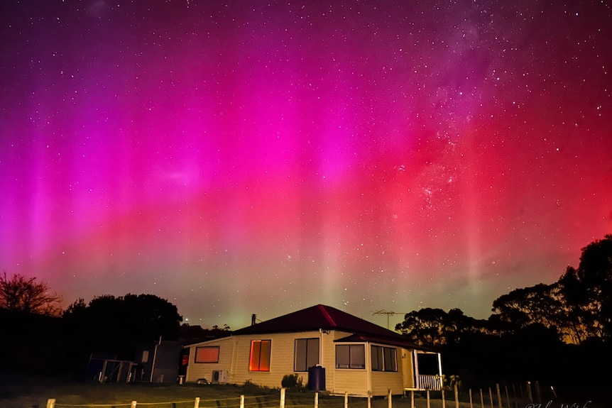 Violet and red lights shines in aurora australis above a house