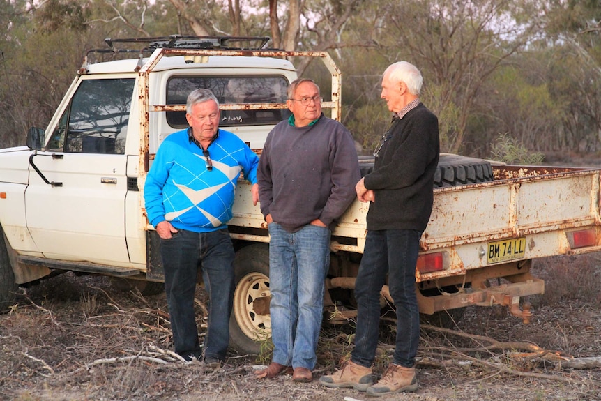 Three men lean on a utility truck
