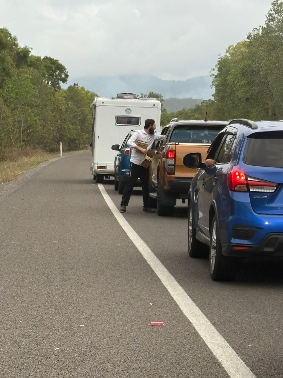 Un hombre con camisa blanca llega a un metro naranja que está atrapado en un atasco y entrega regalos.