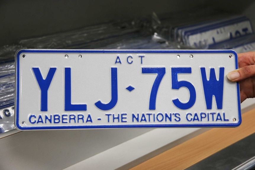A hand holds a new ACT number plate.