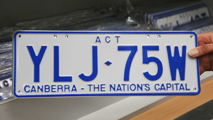 A hand holds a new ACT number plate.