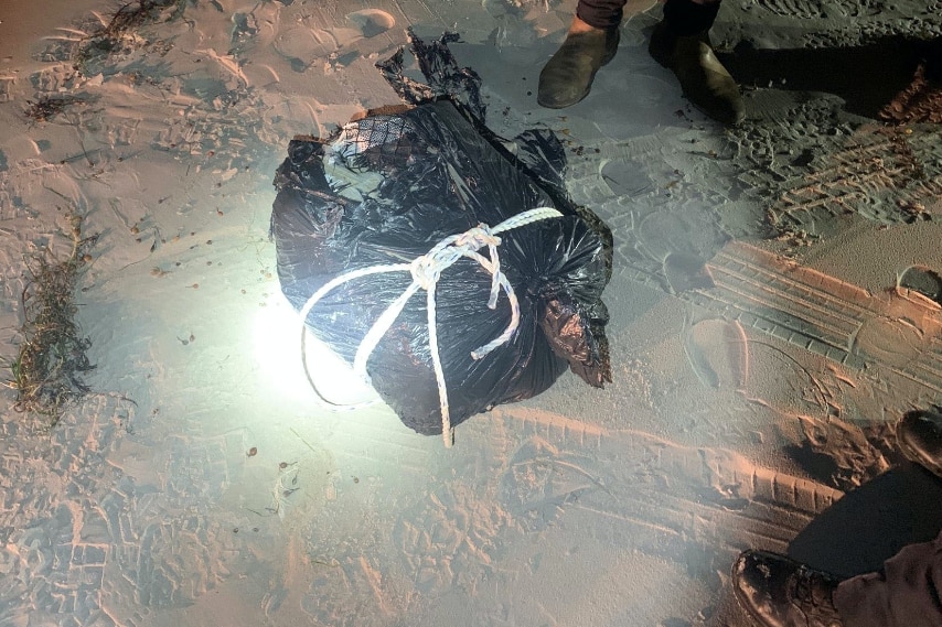 Black plastic bag with white rope on a beach