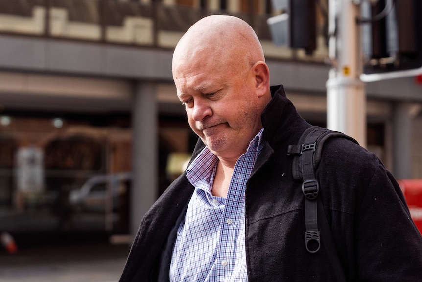 Mr Reynolds carries a bag and walks on the footpath, looking down.