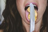 A woman licking peanut butter from a knife.