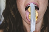 A woman licking peanut butter from a knife.