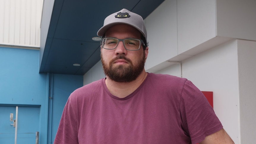 Man with dark beard and glasses in a burgundy t-shirt and cap