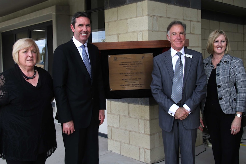 Four people pose for a photo standing either side of a plaque and smiling.