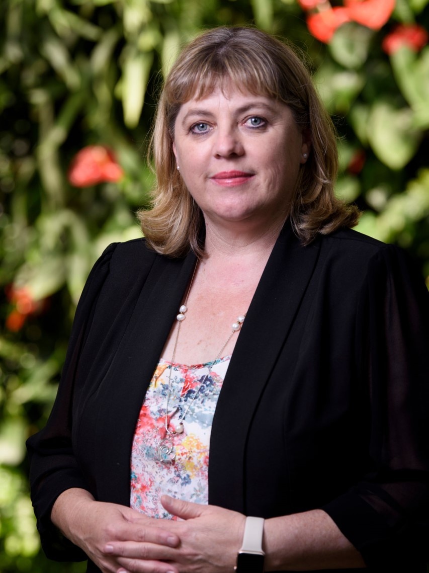 A woman stands with her hands clasped in front of her and a calm expression on her face