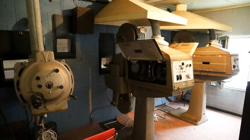 Slide projector and two carbon arc projectors in small grey bricked room