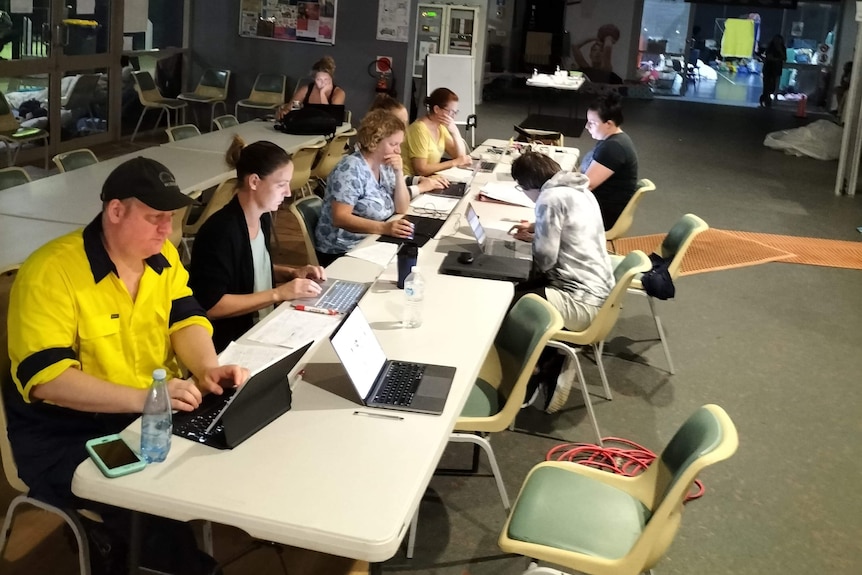 Seven people sit at desks with computers