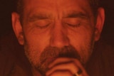 Adam Goodes sits peacefully with his eyes closed near the warm glow of a fire.