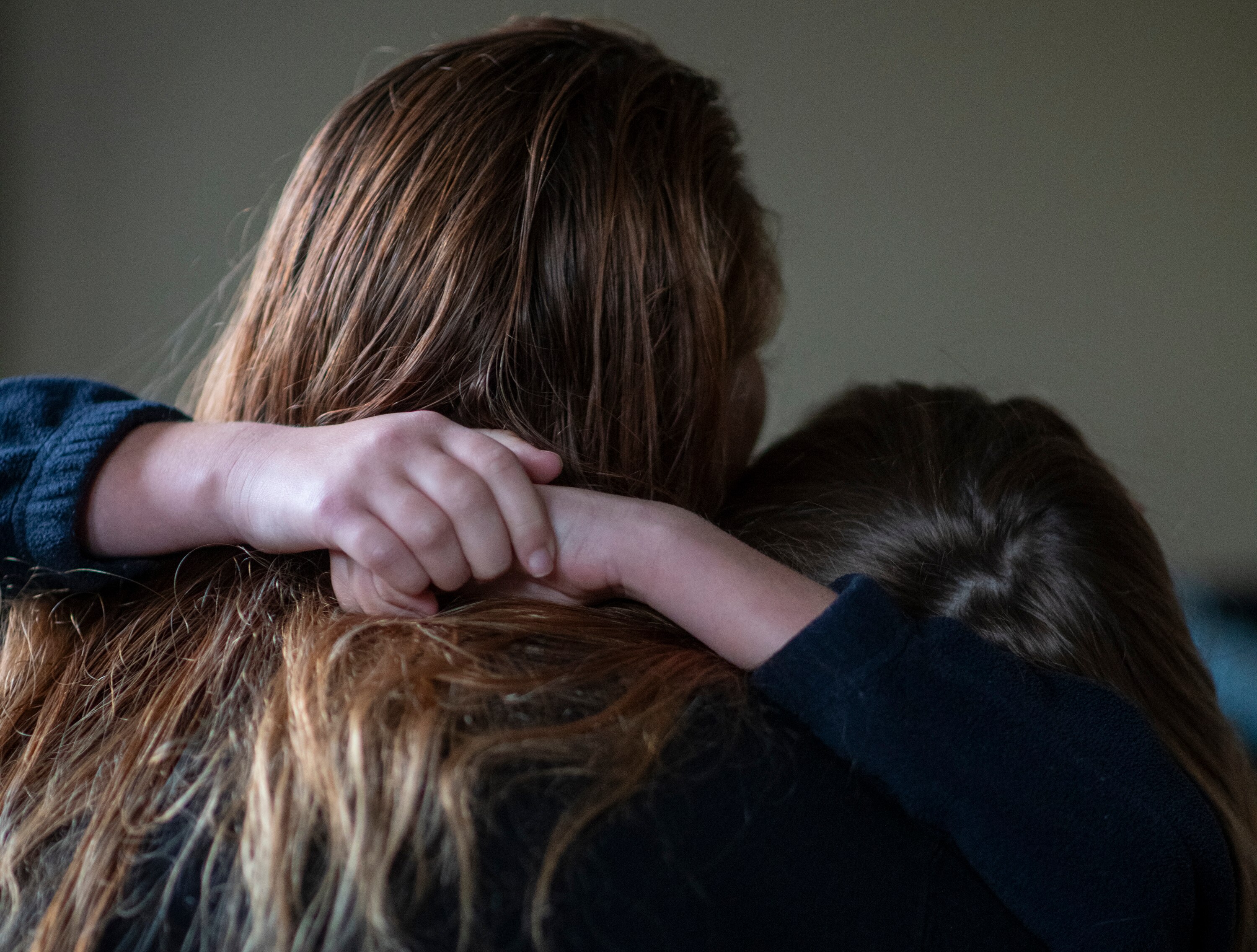 A young girl's hands clasp around her mum's shoulders during an embrace.