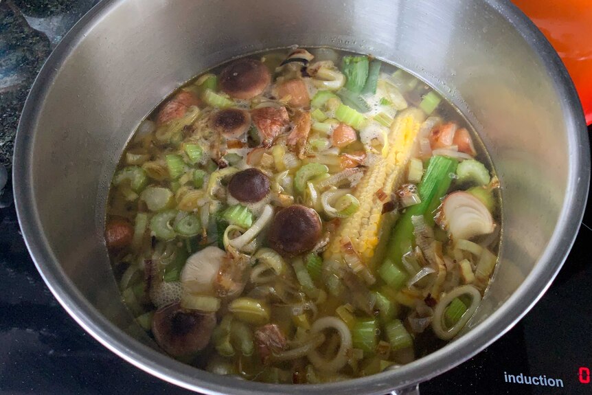 Vegetable stock ingredients simmering in a pot with water, including leeks, garlic, mushrooms, celery and corn cobs.