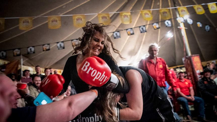 Two women fight it out in the Fred Brophy boxing tent, as spectators look on.