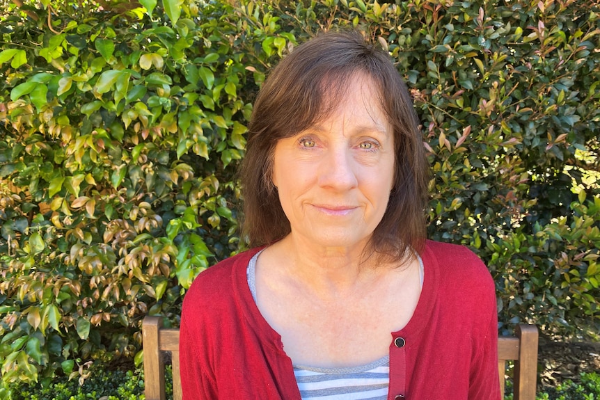 Lesley Hughes sitting outside on a bench smiling.