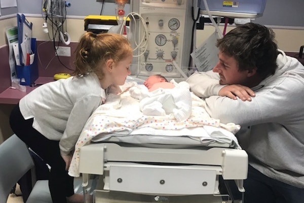 A man and young girl sit at bedside of a newborn baby