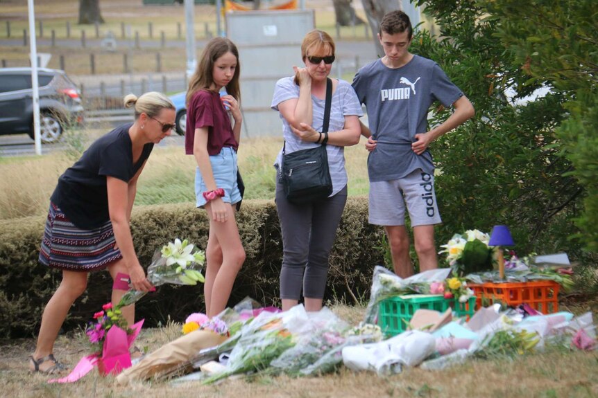 A woman lays a floral tribute Aiia Maasarwe at the site where her body was found, while a woman, a boy and a girl look on.