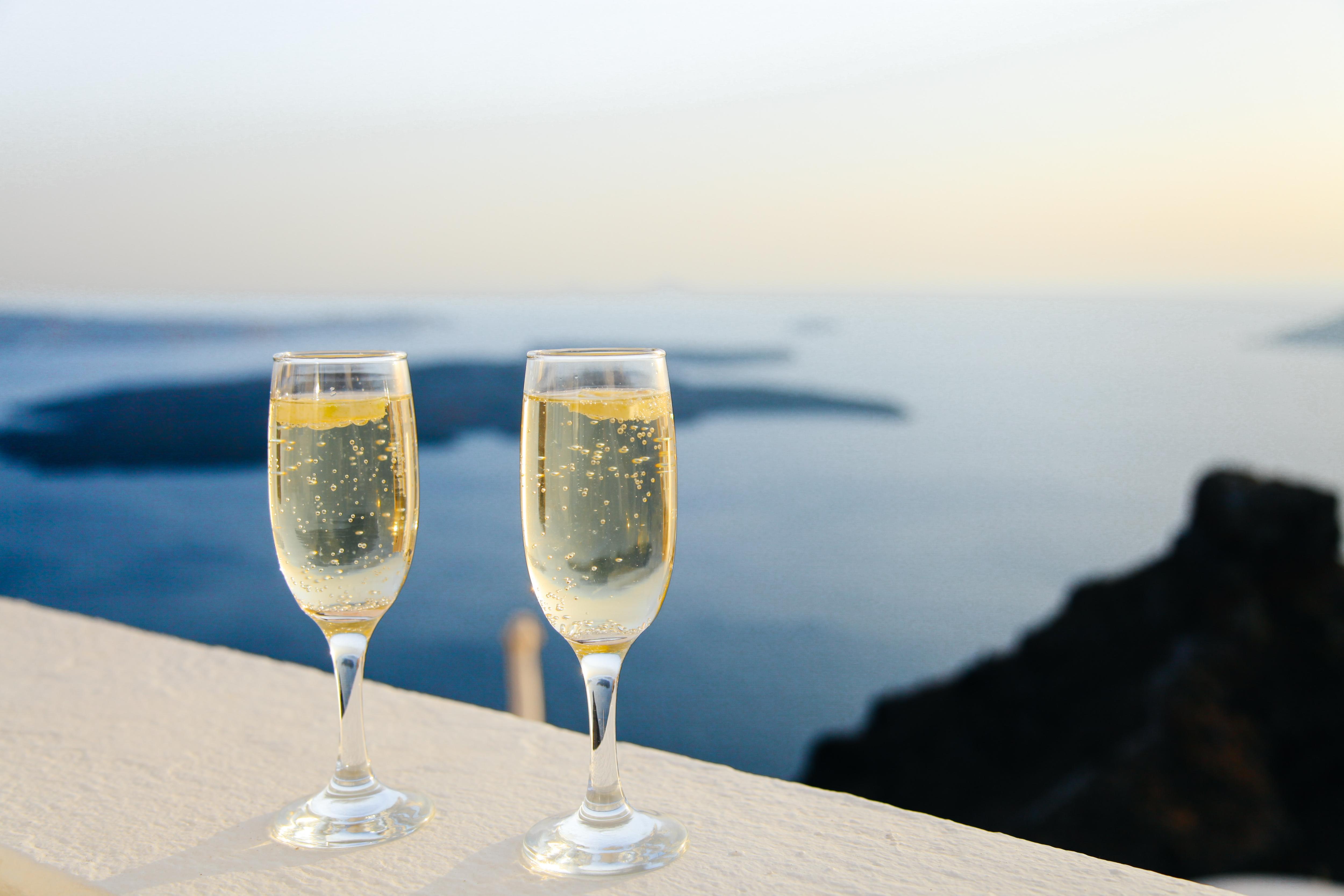 Two glasses of bubbly wine on a bench with water and islands in the background