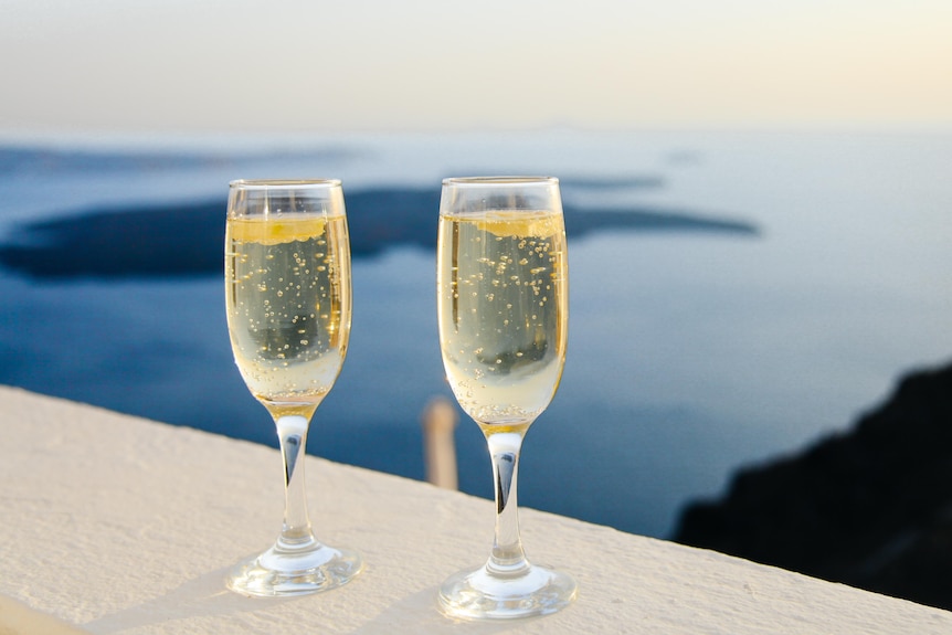 Two glasses of bubbly wine on a bench with water and islands in the background