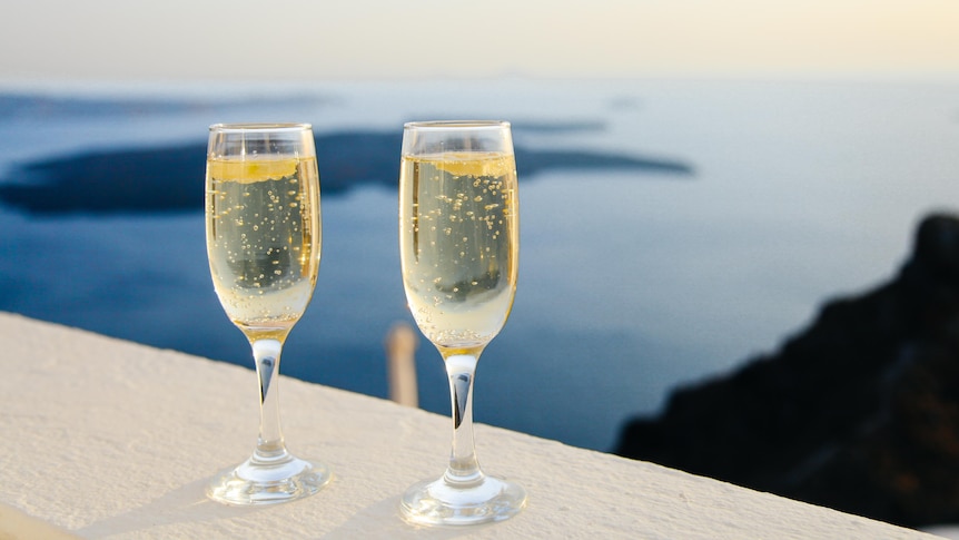 Two glasses of bubbly wine on a bench with water and islands in the background
