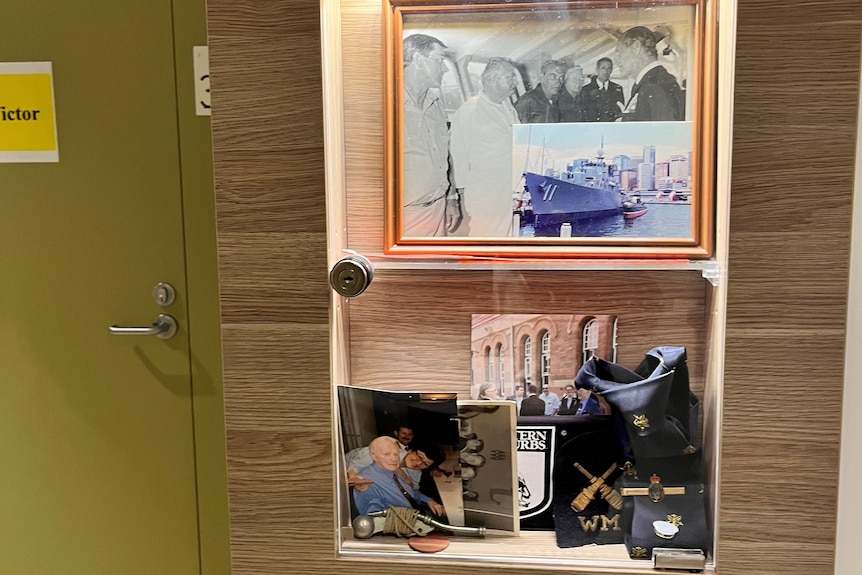 A box attached to a wall near a door, lit up and covered with a clear perspex screen, filled with photos and war medals.