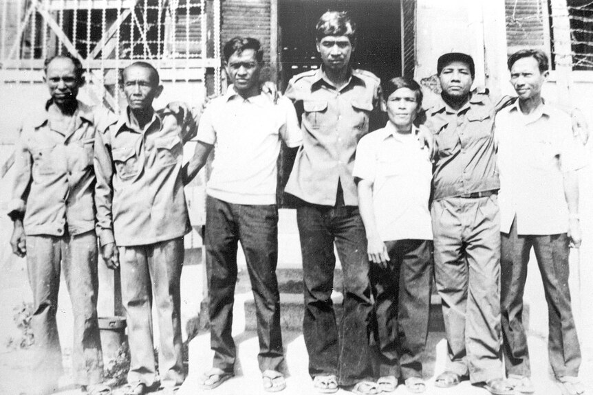 A black and white photo of the seven adult survivors of S-21 pictured standing side by side.
