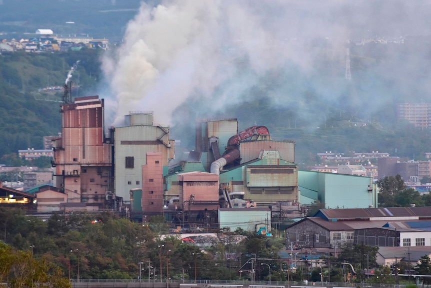 Smoke billows from a large factory, with other buildings nearby.