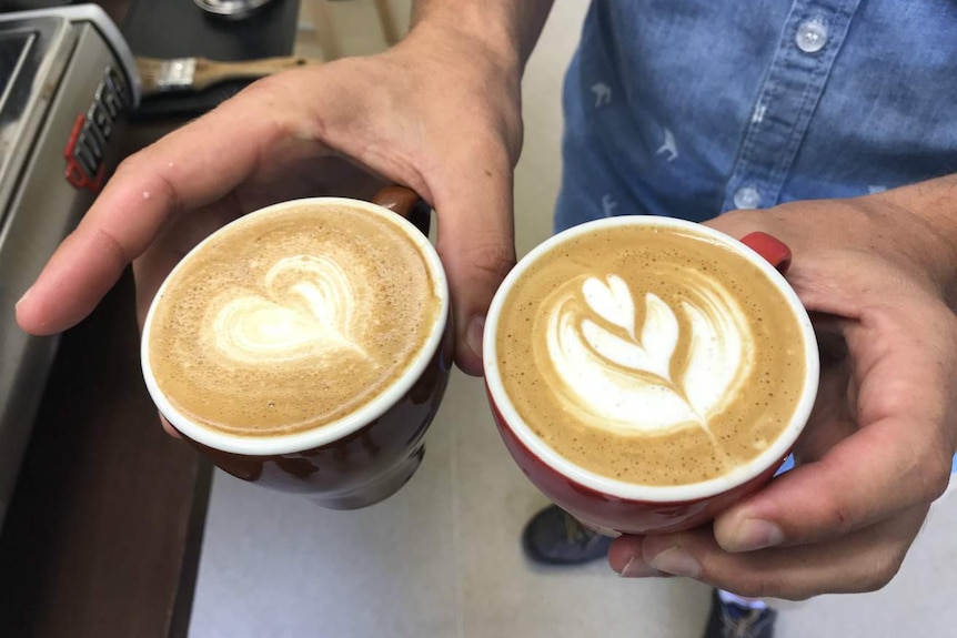 Two beautifully made cups of coffee, one with a heart, the other with a leaf design on it.
