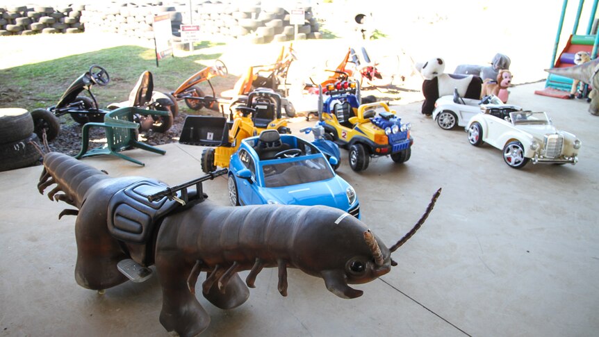 A bevvy of odd rides for children are scattered across a concrete floor