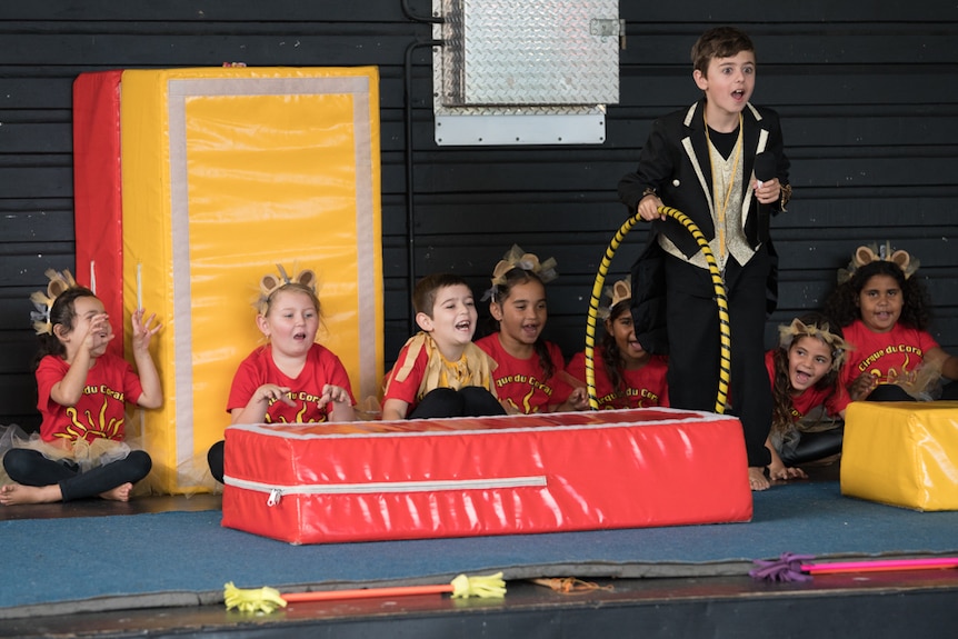 Young boy dressed as a lion tamer performs on stage with other children dressed as lions.