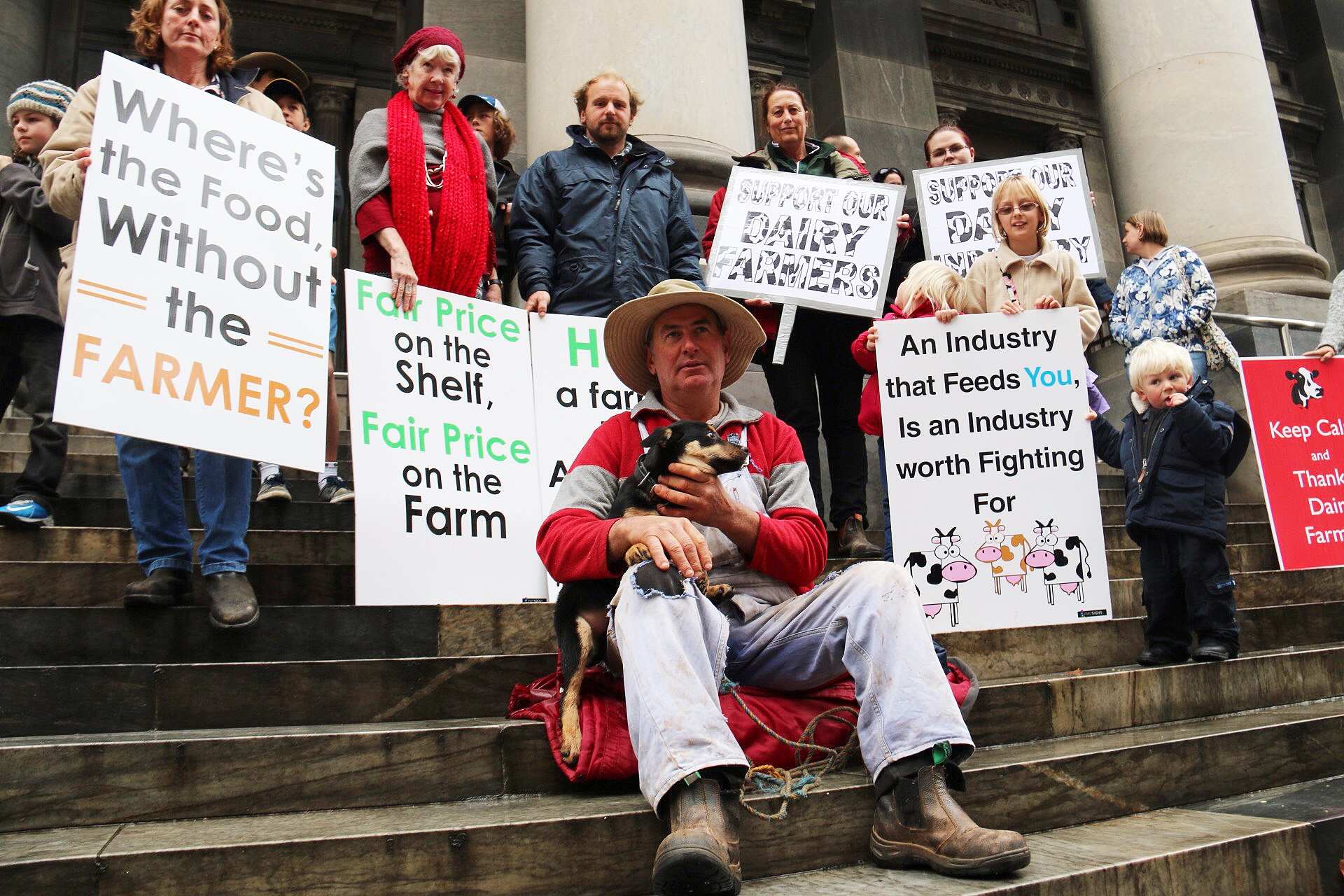 A dozen protestors holding banners supporting dairy farmers on the steps of South Australia's Parliament House in Adelaide