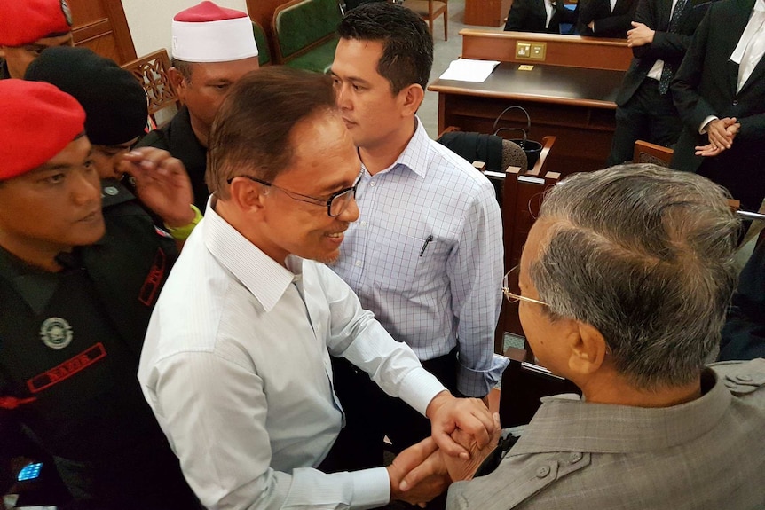 Overhead shot of Anwar Ibrahim and Mahathir Mohamad shaking hands.