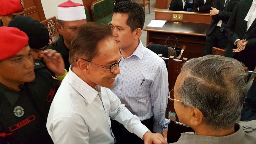 Overhead shot of Anwar Ibrahim and Mahathir Mohamad shaking hands.