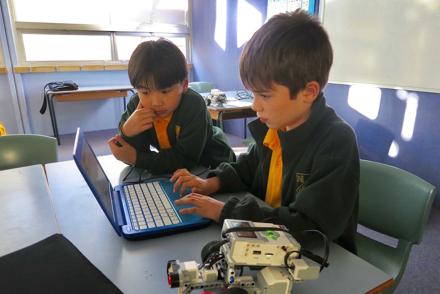 Two male primary school students look at a compute screen in a classroom with a small robot on the table near them