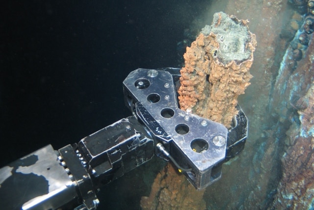 A remotely operated vehicle takes a rock sample underwater.