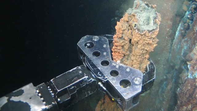 A remotely operated vehicle takes a rock sample underwater.