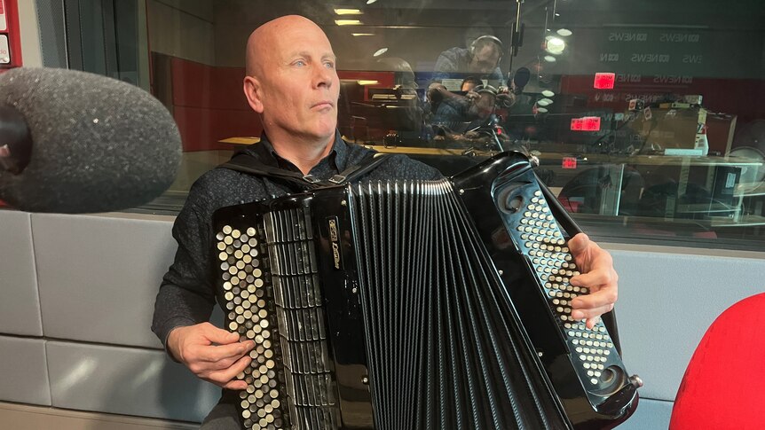 Bald man playing a huge accordion with over 100 buttons for each hand.