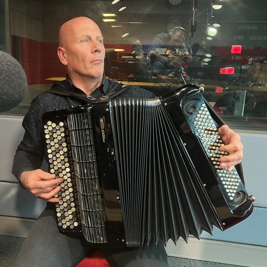 Bald man playing a huge accordion with over 100 buttons for each hand.